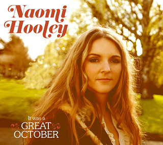 The cover of Naomi Hooley's album, which features a white woman with long blonde hair staring into the camera on a beautiful fall day.