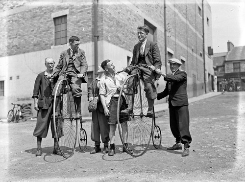 Group of men some wearing plus fours riding penny farthing bicycles