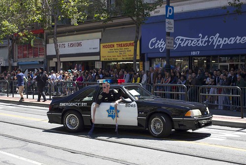 SFPD patrol car, with officer leaning out window, with handfuls of colorful beaded necklaces