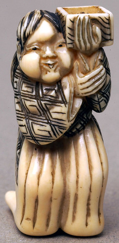 003-Netsuke de Marfil representa a una mujer con el pelo largo recogido hacia atrás con una caja-Bolton Museum and Archive Service