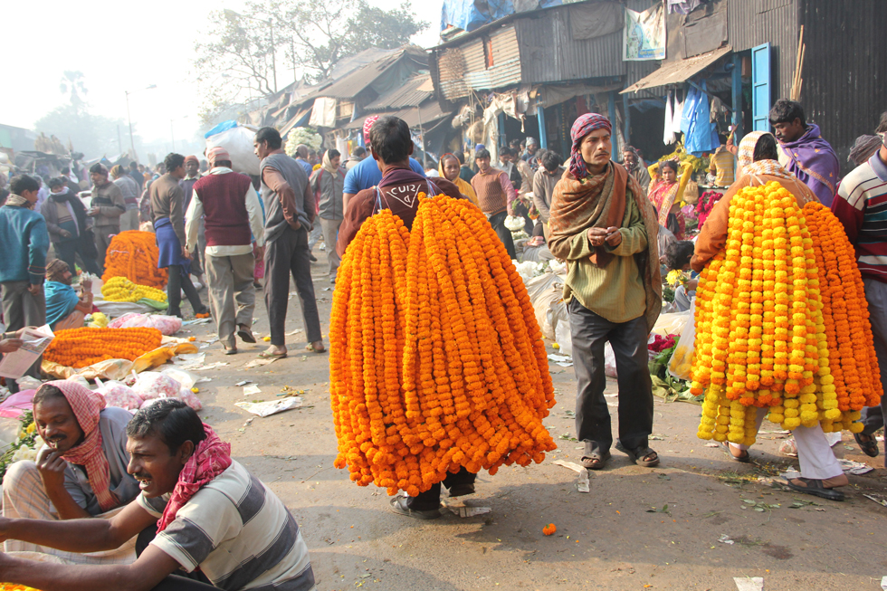 Men walk through the market bearing strands of marigold flowers