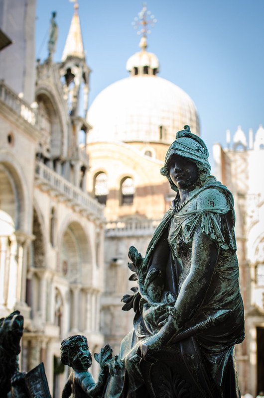 A statue outside the bell tower in St. Mark's Square, the basilica in the background.