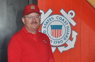 Coast Guard Chief Petty Officer Jesse Meerscheidt poses for a photo in front of a Coast Guard insignia. Meerscheidt pulled a woman from a burning vehicle Oct. 8, 2013, after witnessing a head-on car crash while driving to work. U.S. Coast Guard photograph.