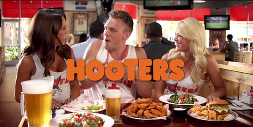 a white guy at a hooters sitting between two waitresses