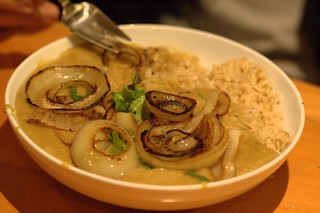 Closeup photo of a bowl full of daal, with fried onions on top and brown rice behind.
