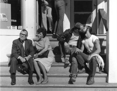 A still photo from We Were Here of a gay couple kissing next to a straight couple who are avoiding looking at them.