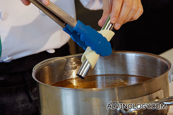 Using a tong to transfer the cannoli into a pot of boiling oil 