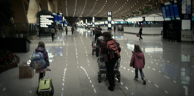 Long Travel - A family walks through an airport with baby carriage and luggage in tow.