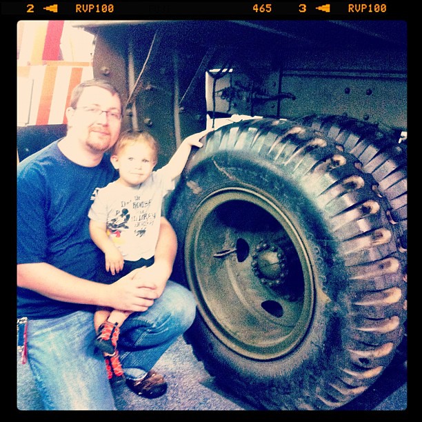 Dad and boy next to the tire of a WW2 tow truck used on the beaches of Normandy.