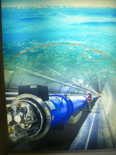 Poster na recepção, mostPoster na recepção, mostrando o anel seccionado do LHC e o túnel, além de um mapa demostrando a extensão do LHC, com os Alpes ao fundo.