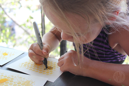 overhead picture of little girl drawing bumble bee onto paper with painted honeycomb 