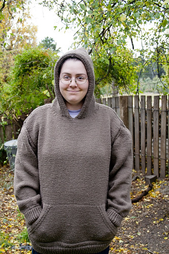 Photo of Ruth wearing the knitted jumper, taken front on with the hood up. You can see the kangaroo pocket on the front