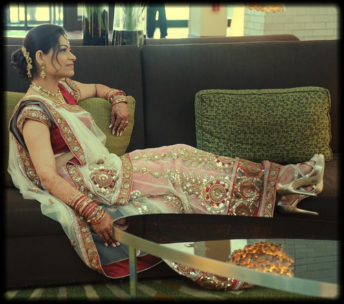 Indian bride relaxing in traditional wedding dress, transparent fabrics, gold patterns, earrings, necklace, henna, bangles, high heel shoes, reflection in the table, Hyatt Regency Hotel, Schaumburg, Illinois, USA by Wonderlane