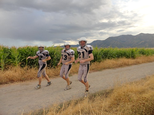 Muddy football players running along corn fields