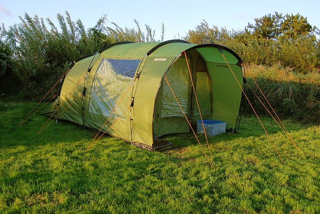 A green tent set up on a campsite