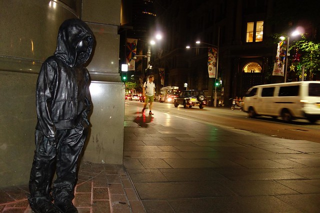 hooded little boy statue looks onto Sydney night time street traffic