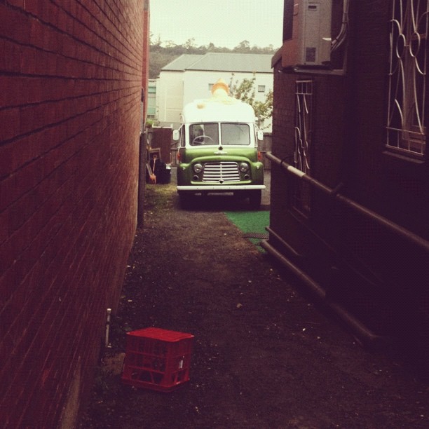 An old ice cream truck hiding in an alleyway.