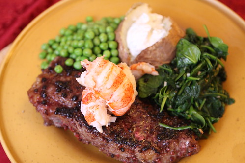 Pink Peppercorn Crusted New York Strip Steak with Lobster Tail, Buttered Peas, Wilted Spinach, and Baked Potato with Horseradish Cream