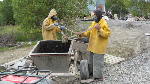 Wearing breathing apparatus, Alaska village residents transfer human waste to a collection bucket.  The untreated waste will then be taken to a sewage lagoon. Working with its partners, USDA is funding projects to replace these systems with safe sewage handling systems, reducing the incidence of disease in Alaska rural villages.