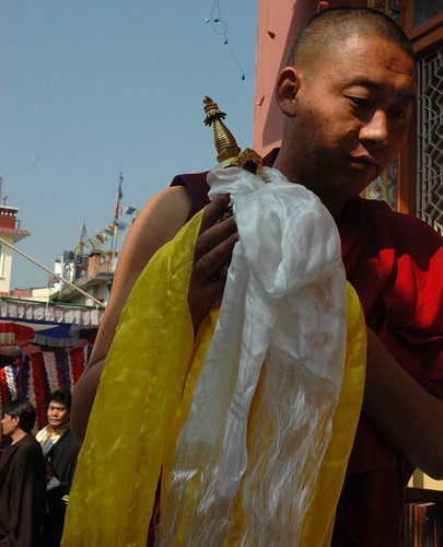 Tibetan monk carries a statue of a stupa as an offering, white and yellow kataks, men wearing chubas in the background, Sakya Lamdre, Tharlam Monastery of Tibetan Buddhism, Boudha, Kathmandu, Nepal by Wonderlane
