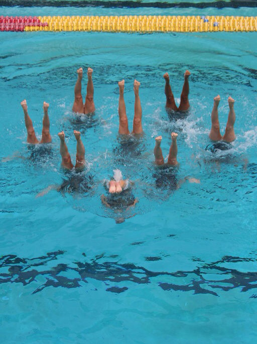 Photo of several synchronized swimmers legs skyward in pool