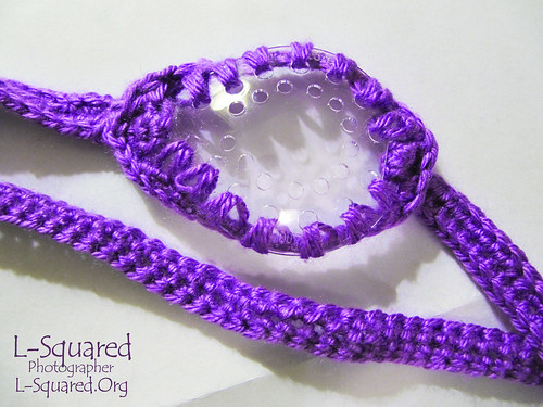 A clear plastic eye shield with a crocheted strap and edging made with bright purple yarn.