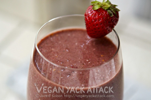 close up of red-violet smoothie in a wine glass, garnished with a strawberry