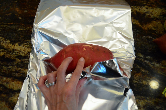 A sweet potato being wrapped in aluminium foil.