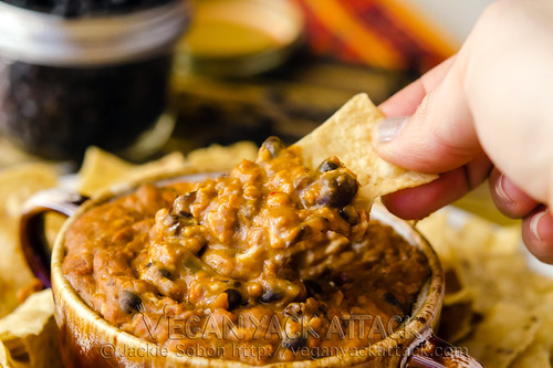 small bowl of cheesy bean soyrizo dip on a plate with chips with hand scooping dip out with chip