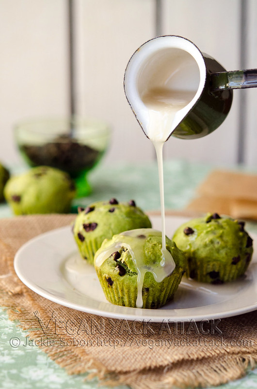 Glaze being poured over green-hued, chocolate chip cupcakes on a plate
