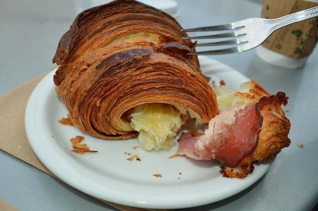 A fork tears open and reveals the center of the ham and cheese croissant.