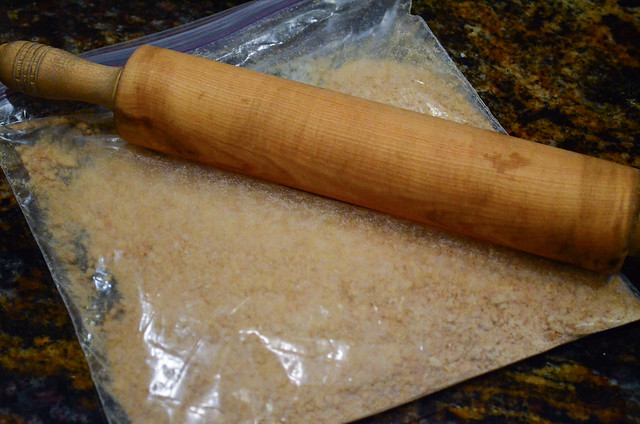 A plastic bag with graham crackers being crushed with a rolling pin.