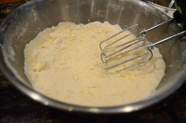 Cake flour, sugar , baking powder, and salt in a bowl with butter being beat in with a hand mixer.