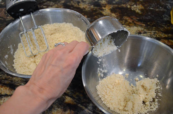 A measuring cup transfer the crumbly mixture into another bowl.