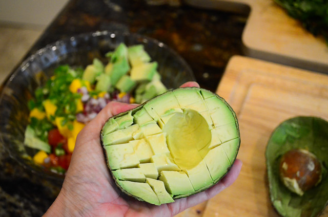An avocado with cuts crosswise and lengthwise being held.