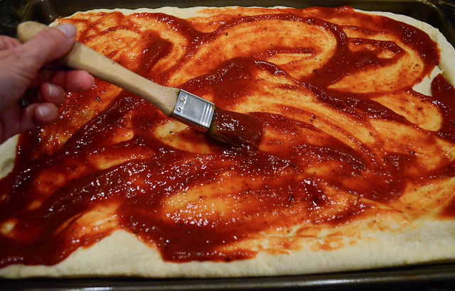 Pizza sauce being spread on top of the pizza dough.