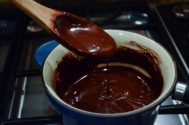 A wooden spoon with melted chocolate drizzling into a pan.