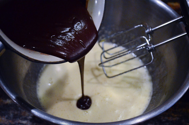 Melted chocolate being poured into a bowl of wet ingredients.