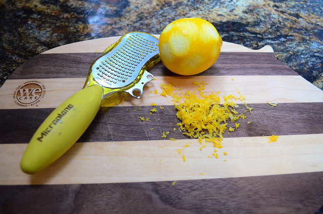 A zester tool laying next to a lemon and pile of lemon zest.