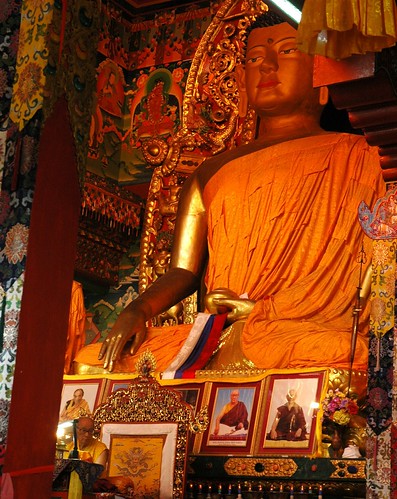 Large statue of Lord Buddha in Earth Touching mudra, red white and blue represent Sakya, with His Holiness Dagchen Sakya seated on his throne, Sakya Lamdre, Tharlam Monastery of Tibetan Buddhism, Boudha, Kathmandu, Nepal by Wonderlane