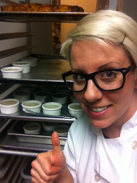 Blonde woman with glasses and thumbs up next to a speed rack of creme brûlée 