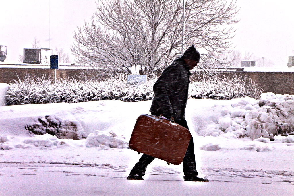 Man-with-suitcase-walking-in-snow-towards-Greyhound-station--Kansas-City