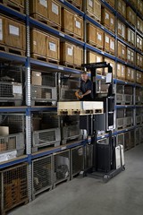 Un operario usa un recogepedidos de nivel medio para recoger mercancías del tercer nivel de la estantería.