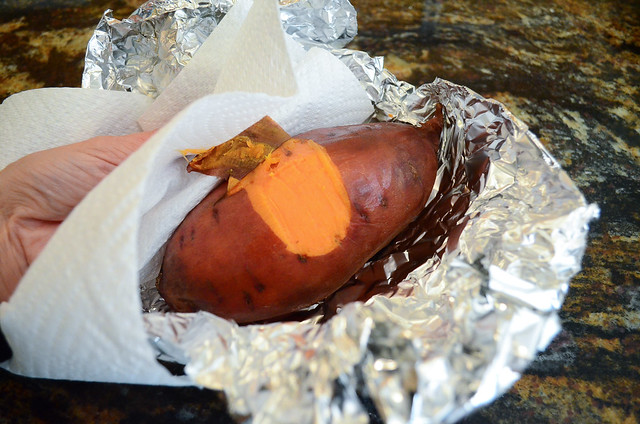 A cooked sweet potato with the skin being removed with a paper towel.