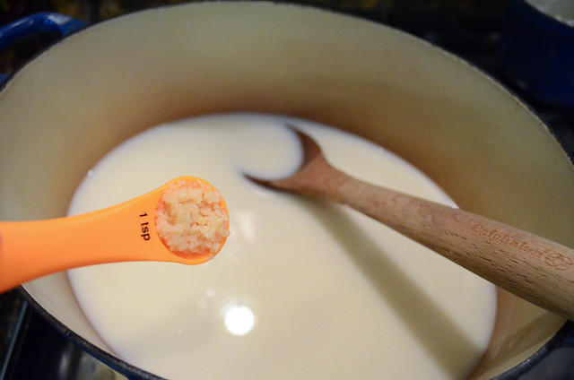 A measuring spoon adding minced garlic to the pot.