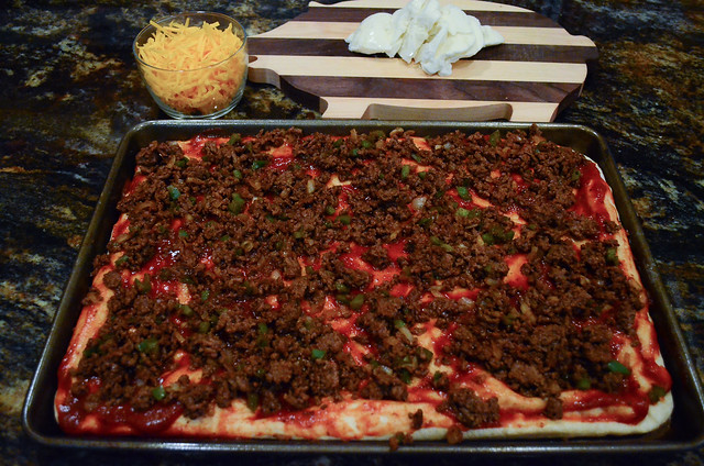 The ground beef is spooned on top of the pizza.