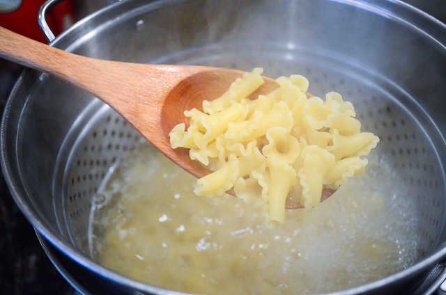 A spoon lifting cooked Campanelle out of a boiling pot.