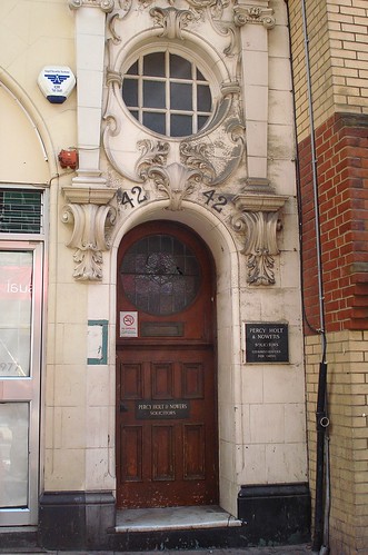 A narrow arched doorway with a porthole window above.  Decorative moulding surrounds the window and the top of the door.