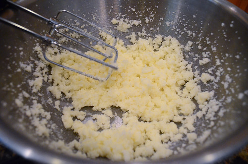 The crumbly mixture of ingredients being mixed together with a hand mixer.