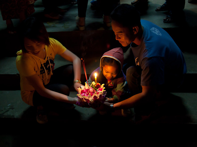Thai couple and child ready to set their candle-lit krathong into the river during Loy Krathong